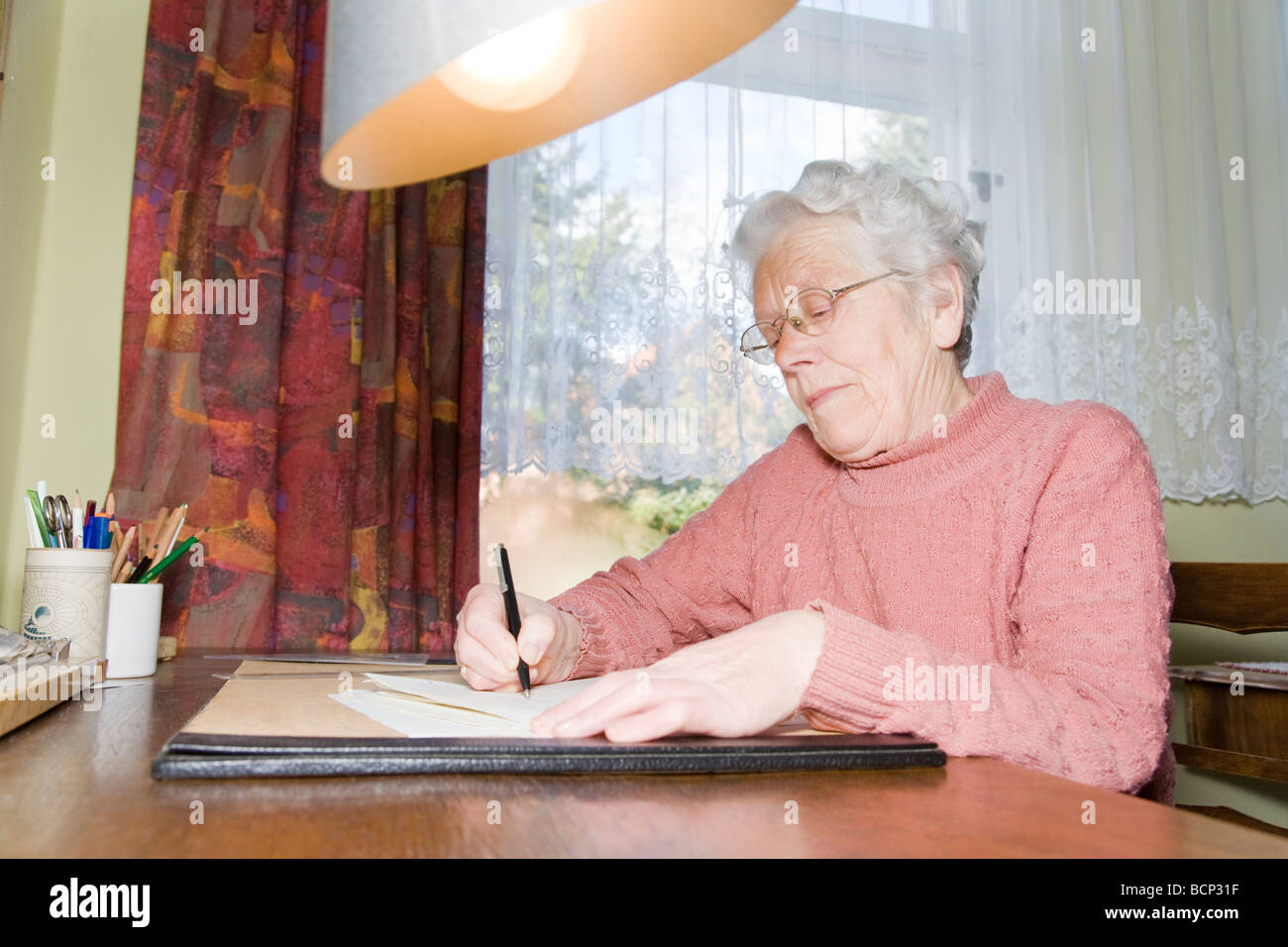 Frau in ihren Siebzigern sitzt am Schreibtisch und schreibt einen Brief Stock Photo