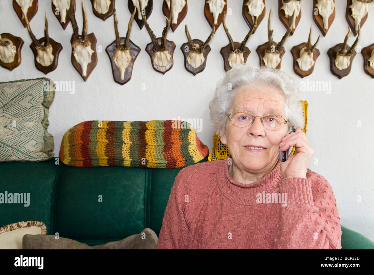 Frau in ihren Siebzigern sitzt auf einem Sofa im Wohnzimmer und telefoniert mit einem Handy Stock Photo
