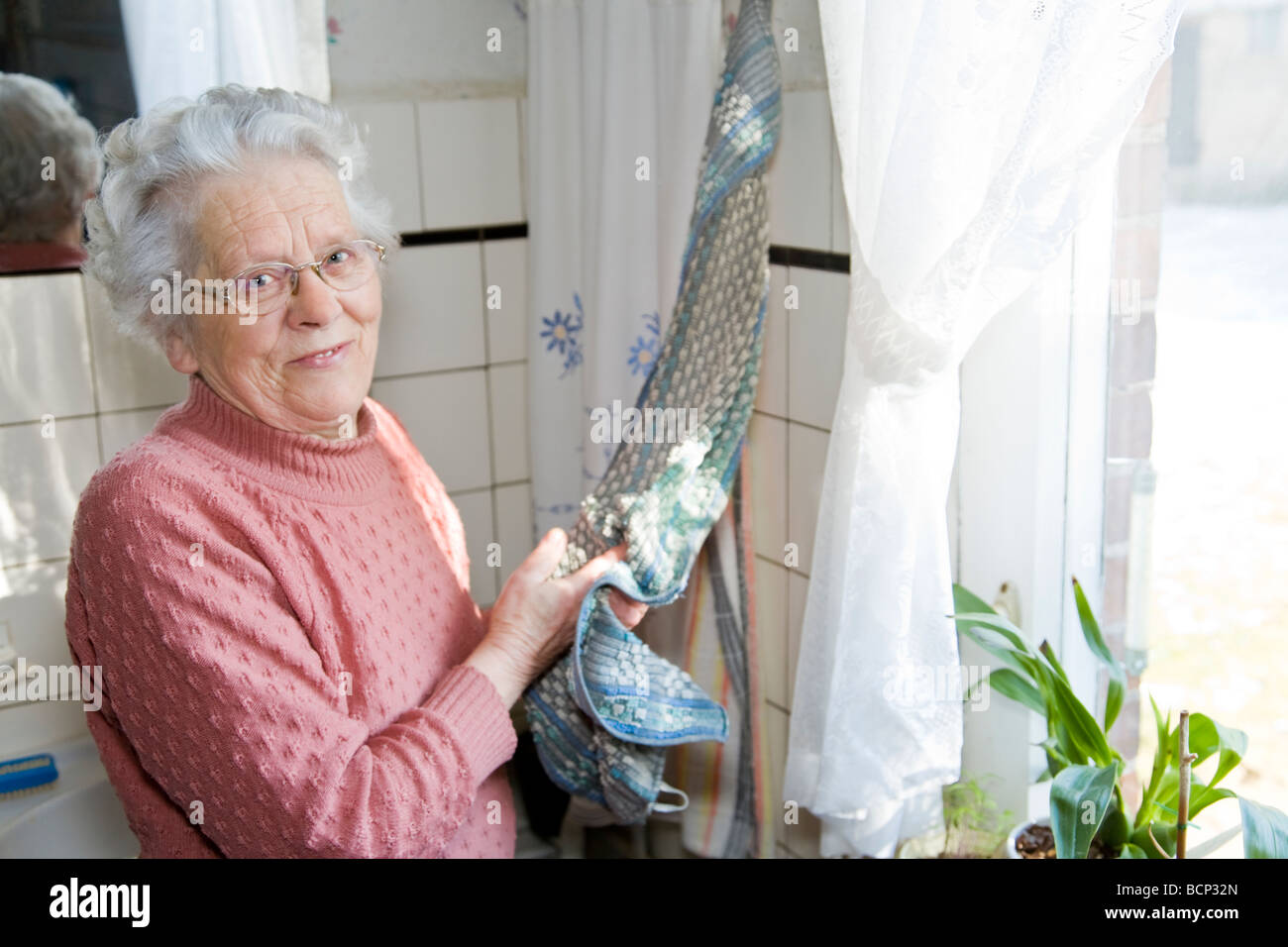 Frau in ihren Siebzigern steht in der Küche und trocknet sich die Hände ab Stock Photo