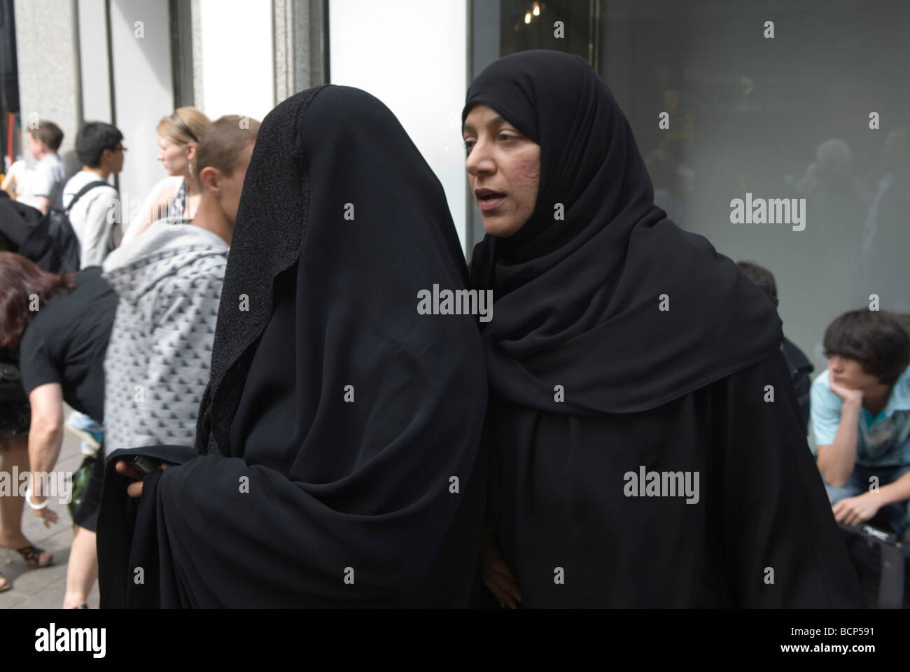 Muslim women wearing full face covered up, a burqa and her friend without face covering chatting. London England 2009 2000s UK. HOMER SYKES Stock Photo