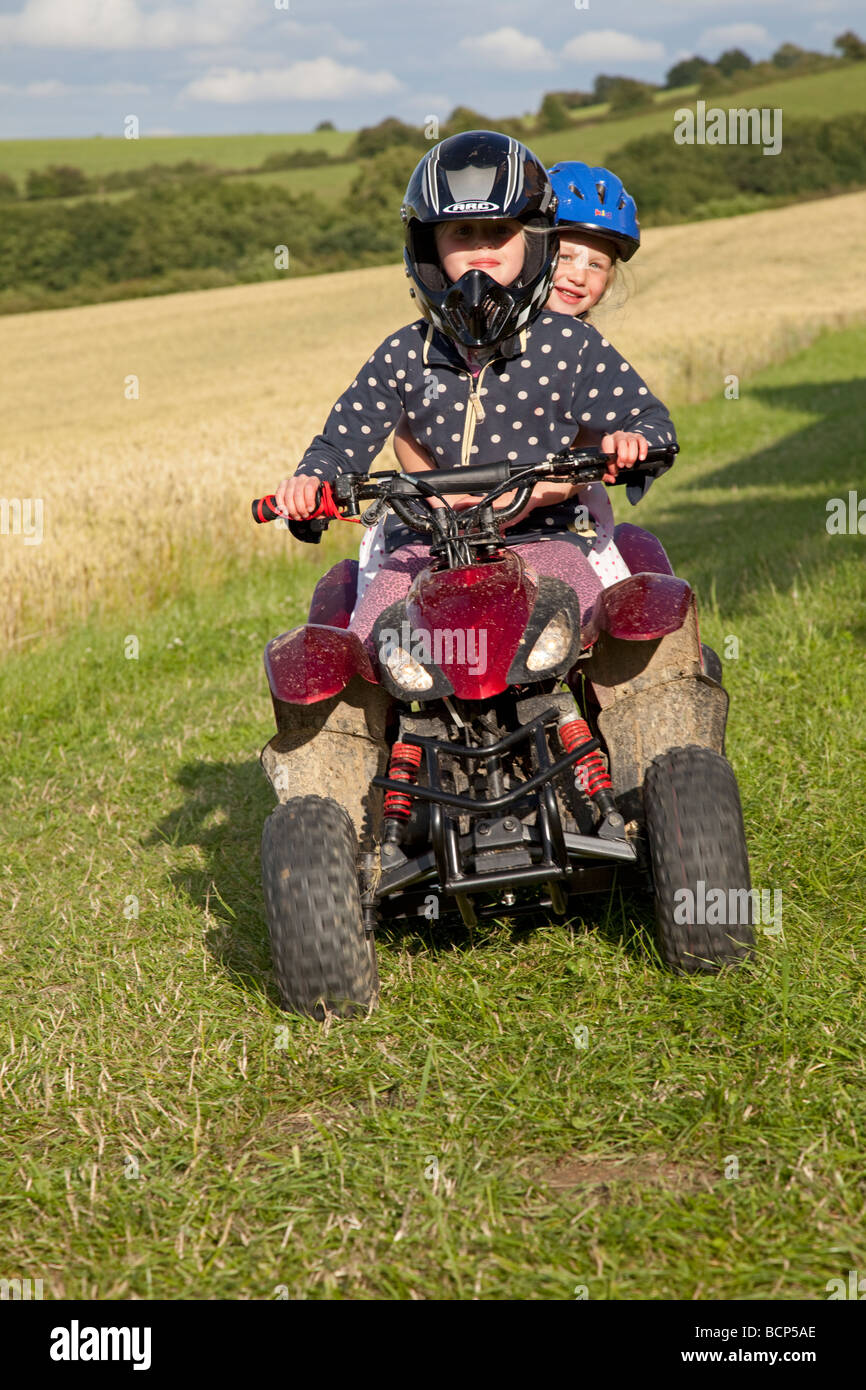 Two girls riding small quad bike farm field Cotswolds UK Stock Photo