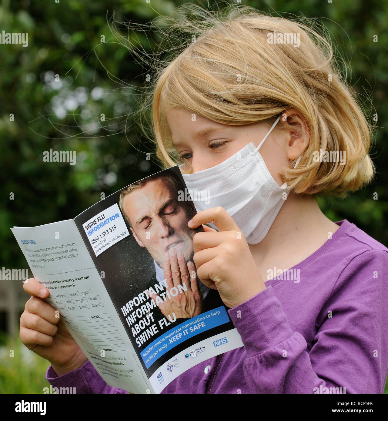 Swine flu information leaflet being read by a little girl wearing a medical mask Stock Photo