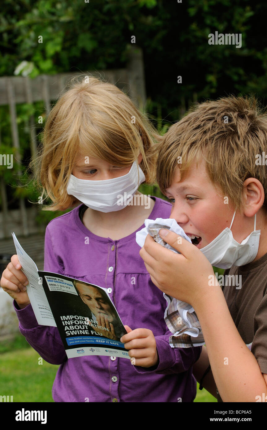 Swine flu information leaflet being read by a little girl and an older boy wearing medical masks Stock Photo