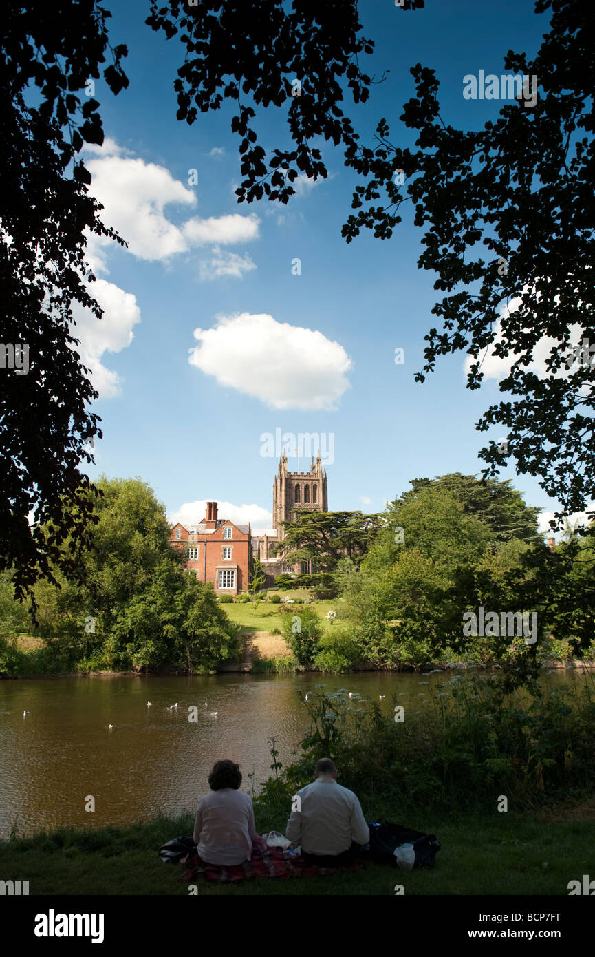 Hereford Cathedral, two people sitting on the banks of the River Wye in  Hereford city Herefordshire England UK Stock Photo
