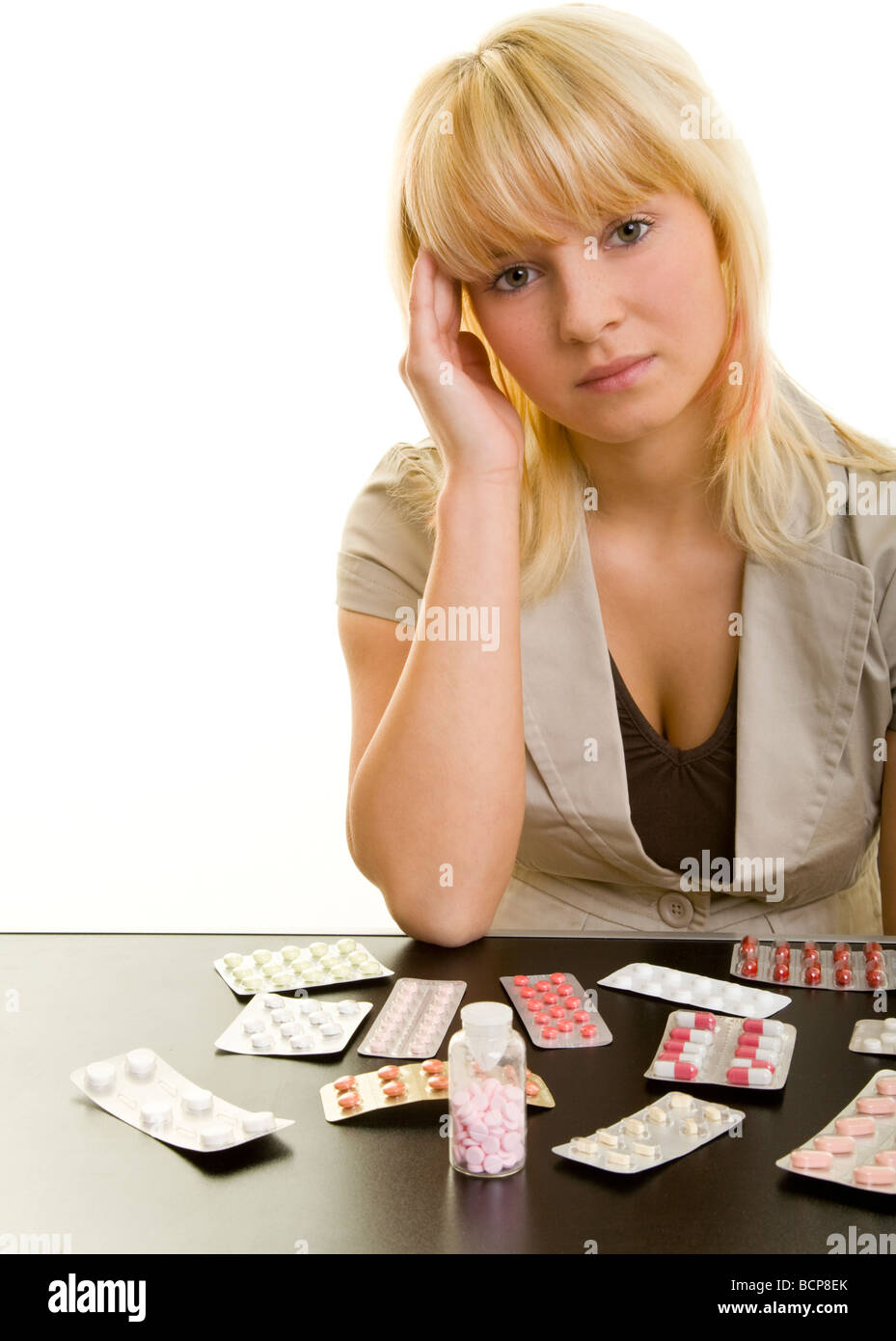Junge Frau mit Kopfschmerzen sitzt an einem Tisch mit vielen Arzneimitteln Stock Photo
