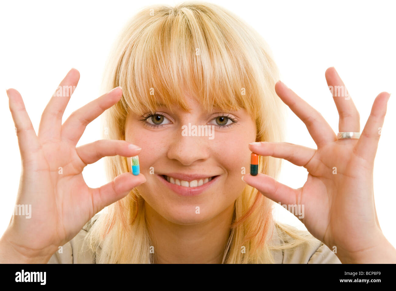 Junge Frau hält lachend zwei verschiedene Kapseln zwischen ihren Fingern Stock Photo