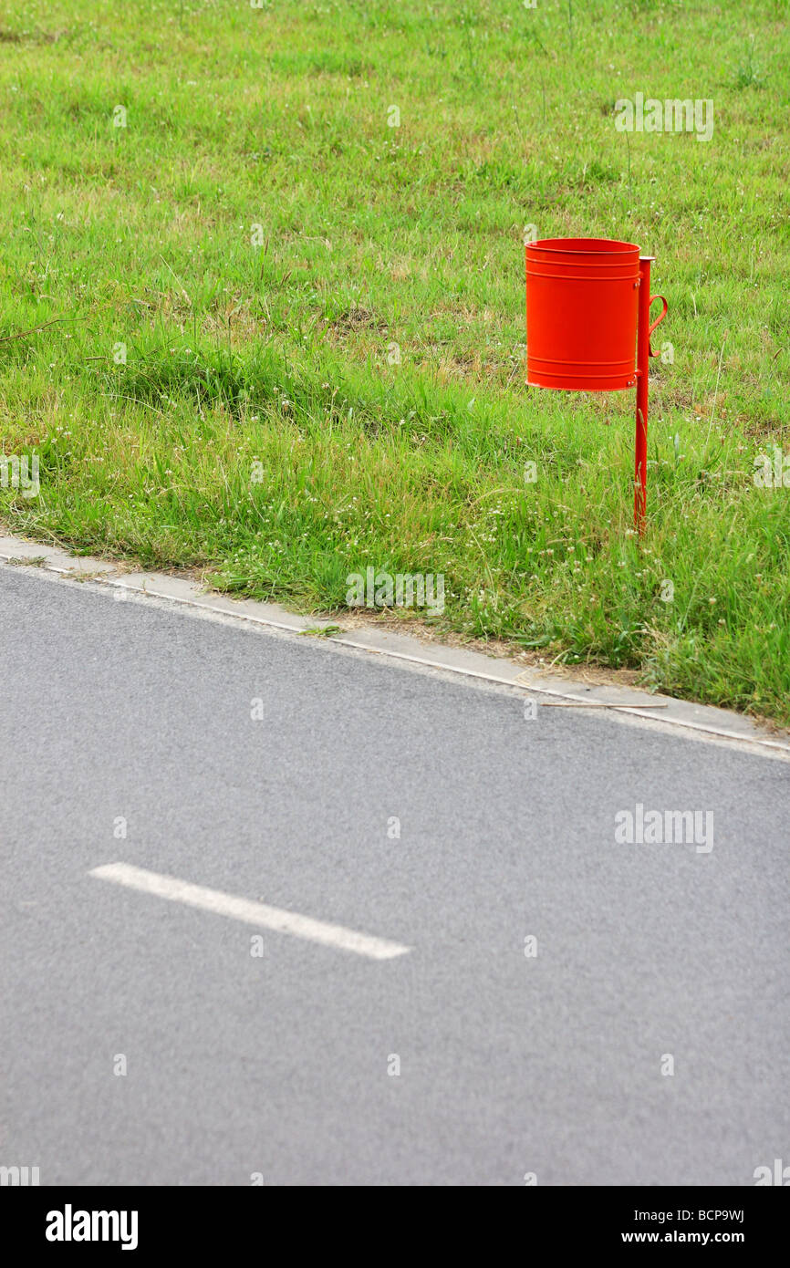 red garbage can on the grass by the road Stock Photo