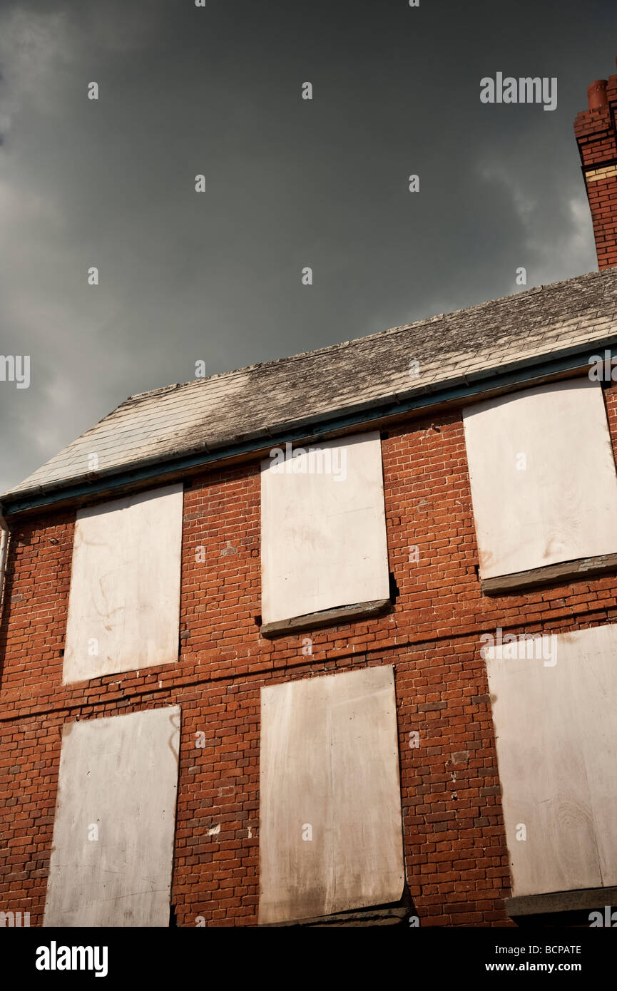 Dark brooding clouds over Boarded up windows of a house building in the ...