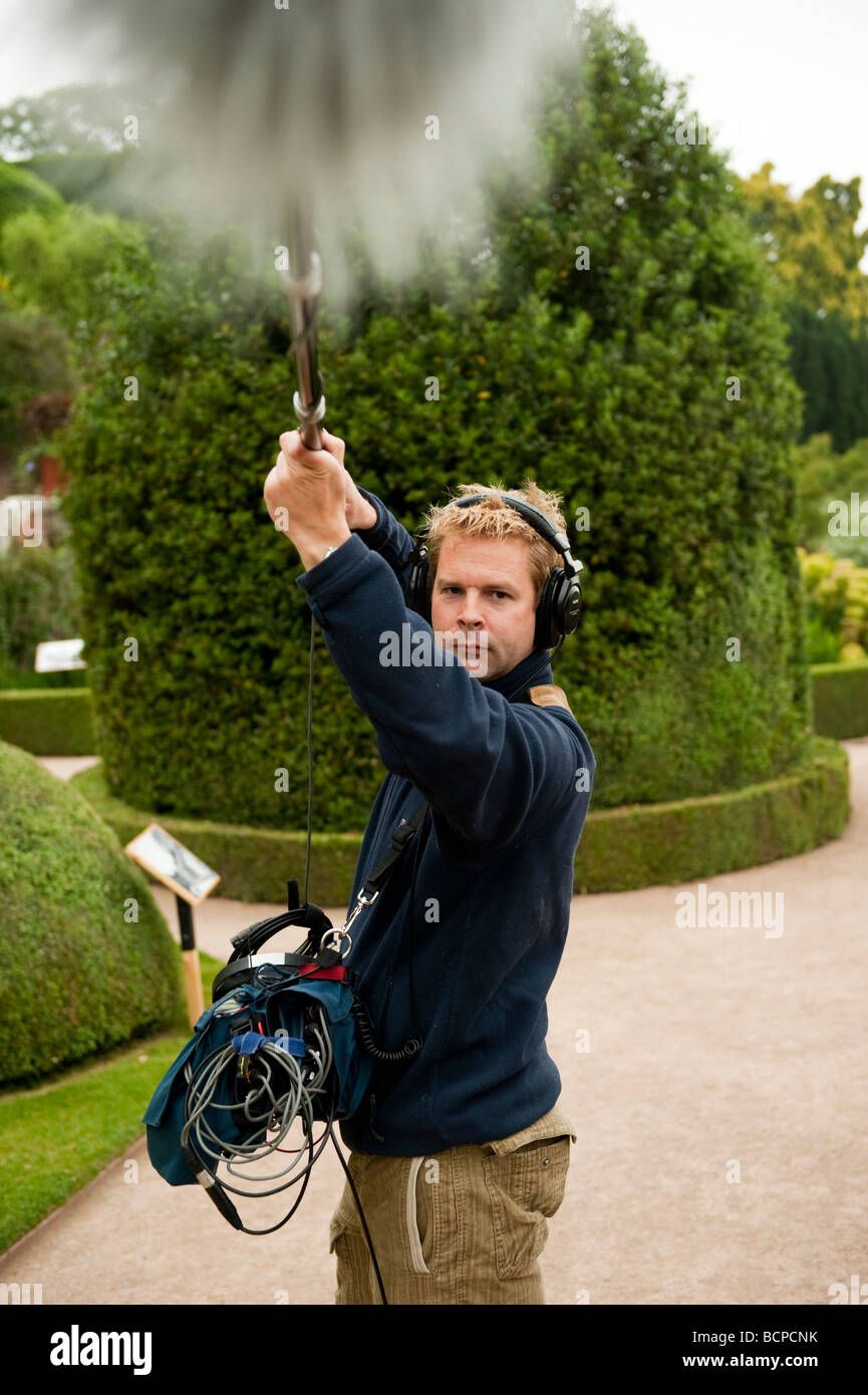 A freelance self employed professional sound recordist recording audio for a television programme holding a microphone on a boom Stock Photo