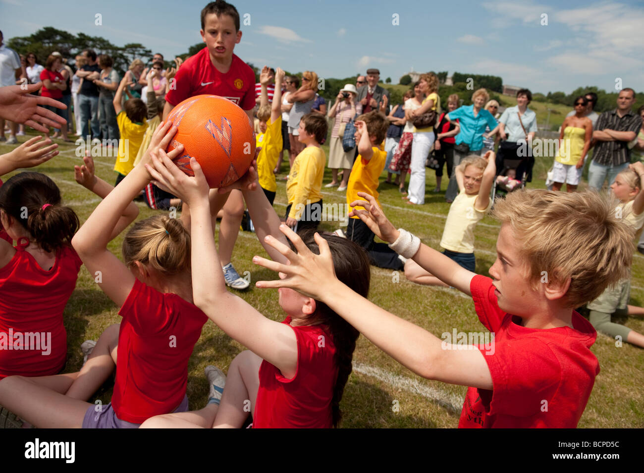 teams of young Children competing at passing a ball backwards over their heads at a Primary School sports day UK Stock Photo