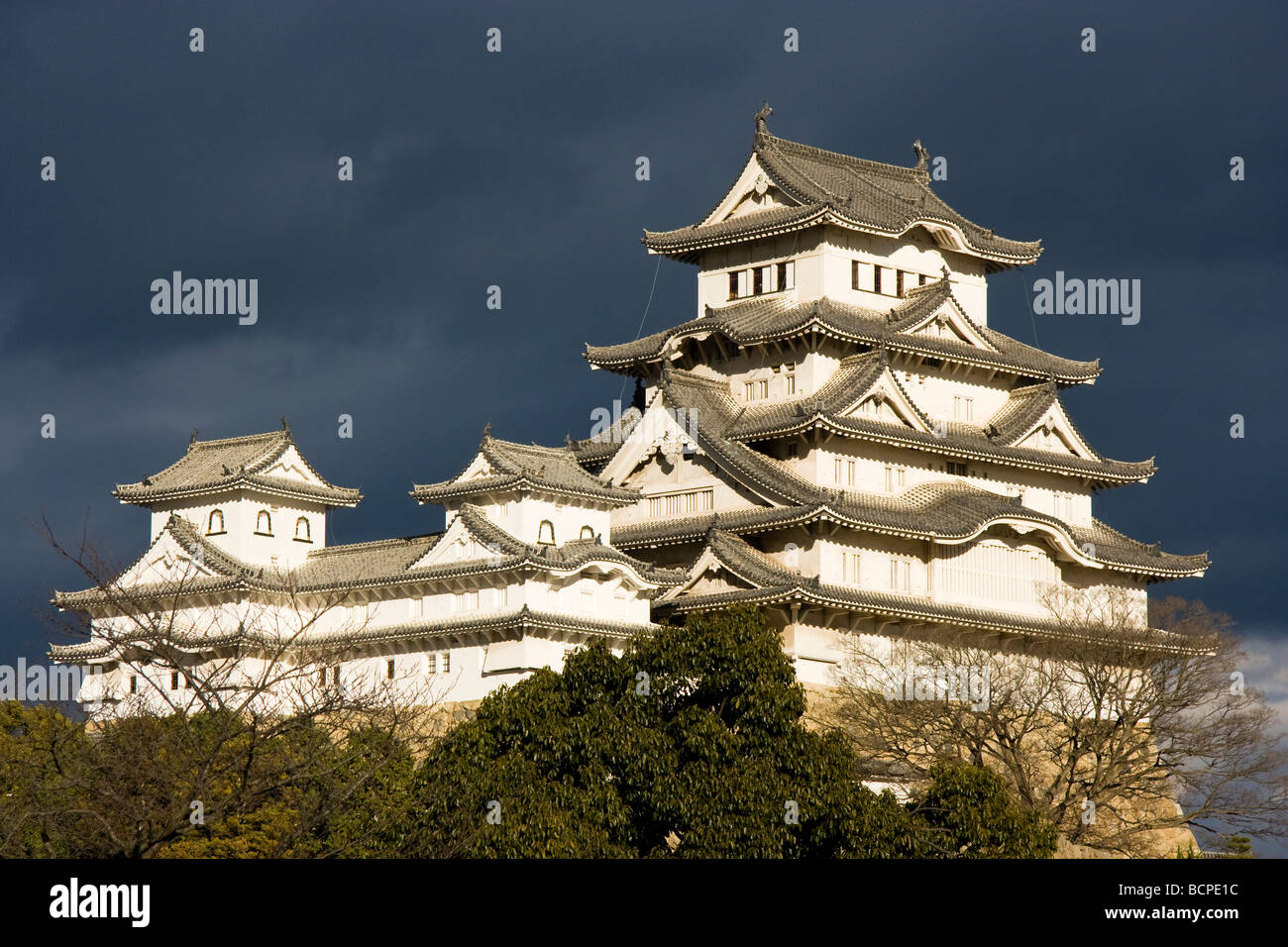 The renritsushiki type keep of Himeji castle, standing out by being lit up by  strong sunlight with against dark grey stormy clouds behind. Stock Photo