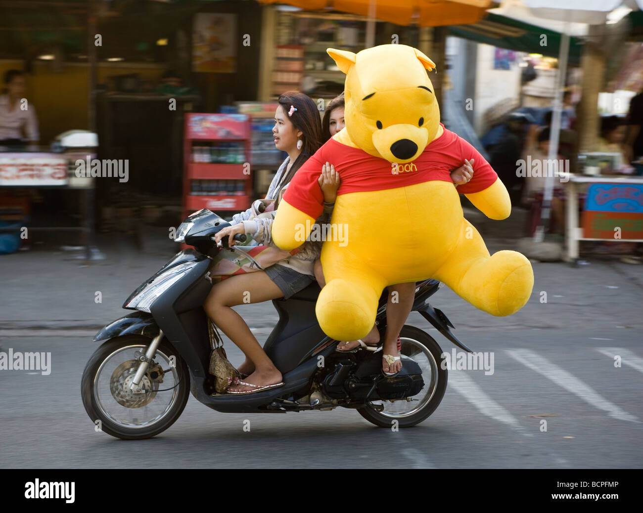 Girl Carrying Huge Wiinie the Pooh Bear on back of motorcycle Phnom Penh Cambodia Cambodian Stock Photo
