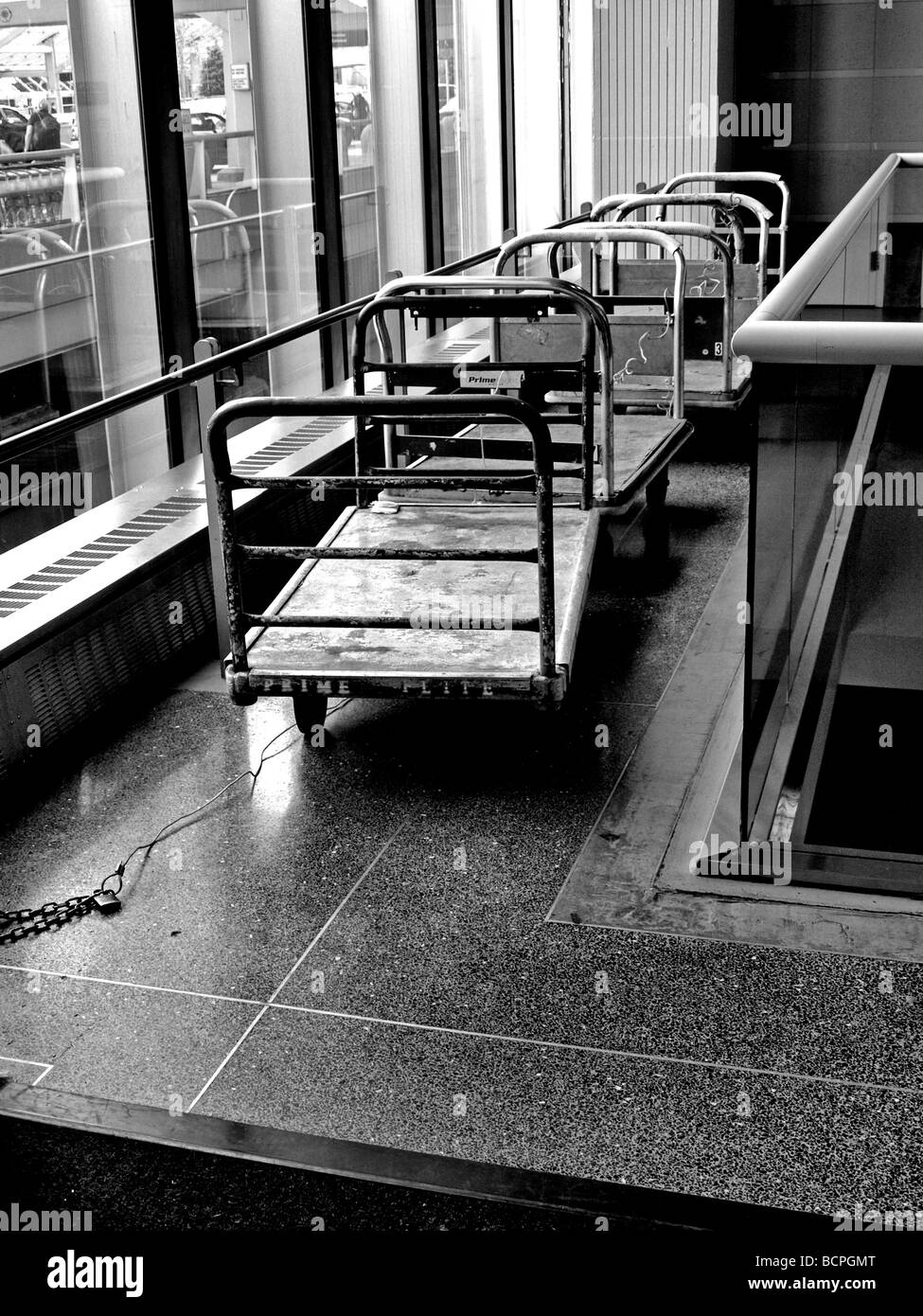 black and white luggage baggage carts used in airport terminal, next to outside windows Stock Photo