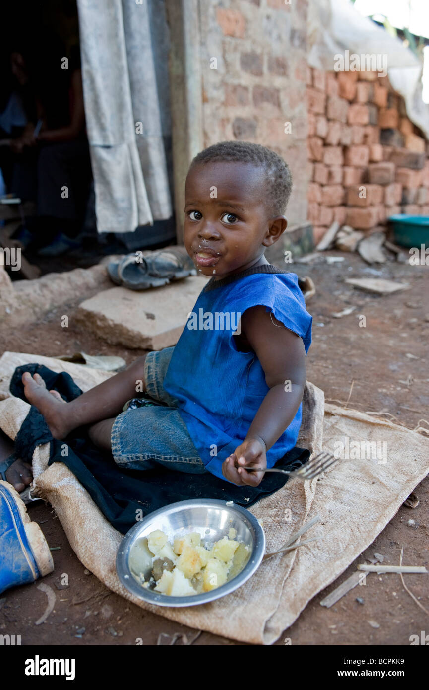 Small boy in blue eating on floor in slum in Uganda Stock Photo