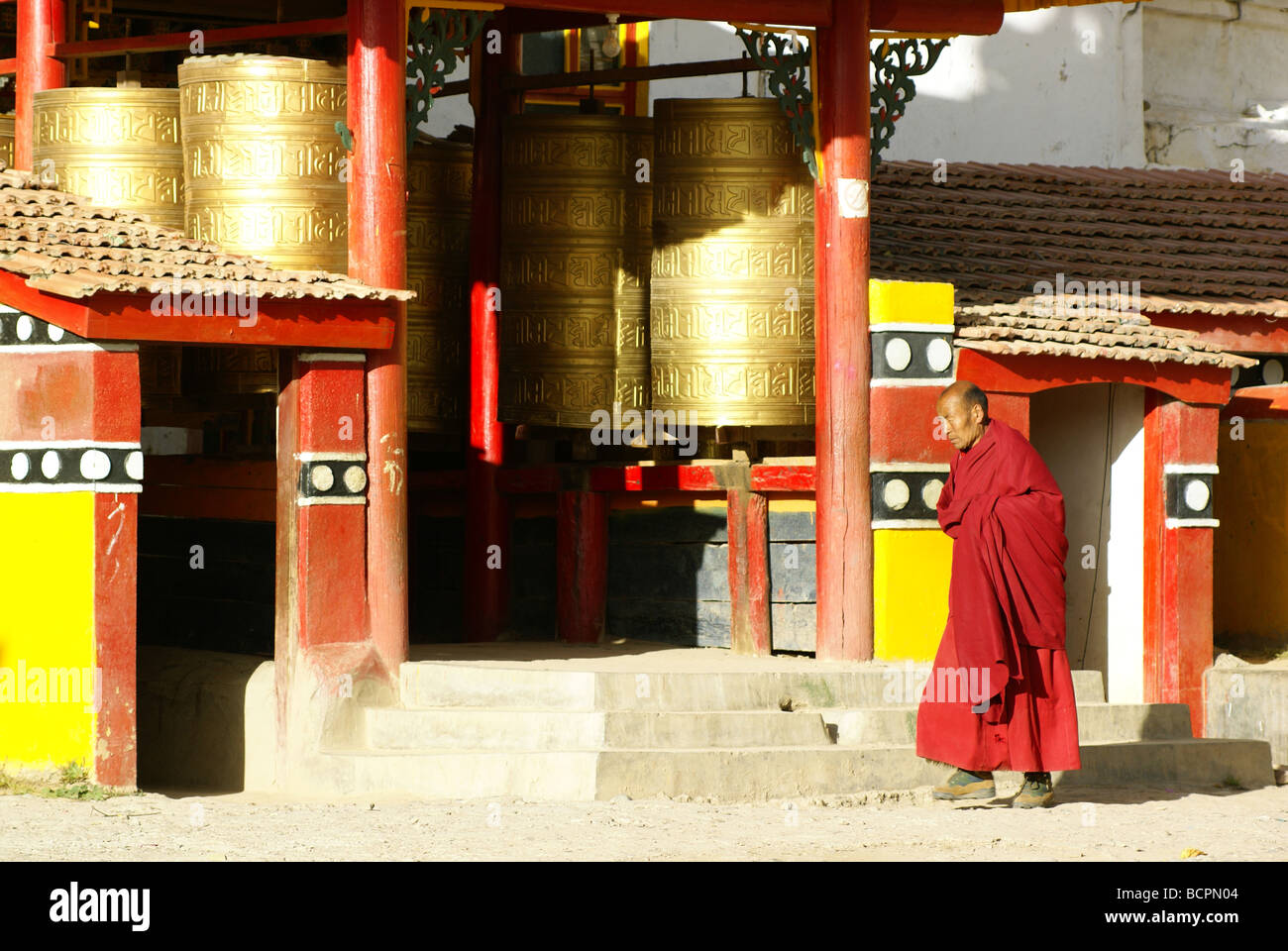Elerly monk walk past gold gilded praying wheels, Geerdeng Monastery