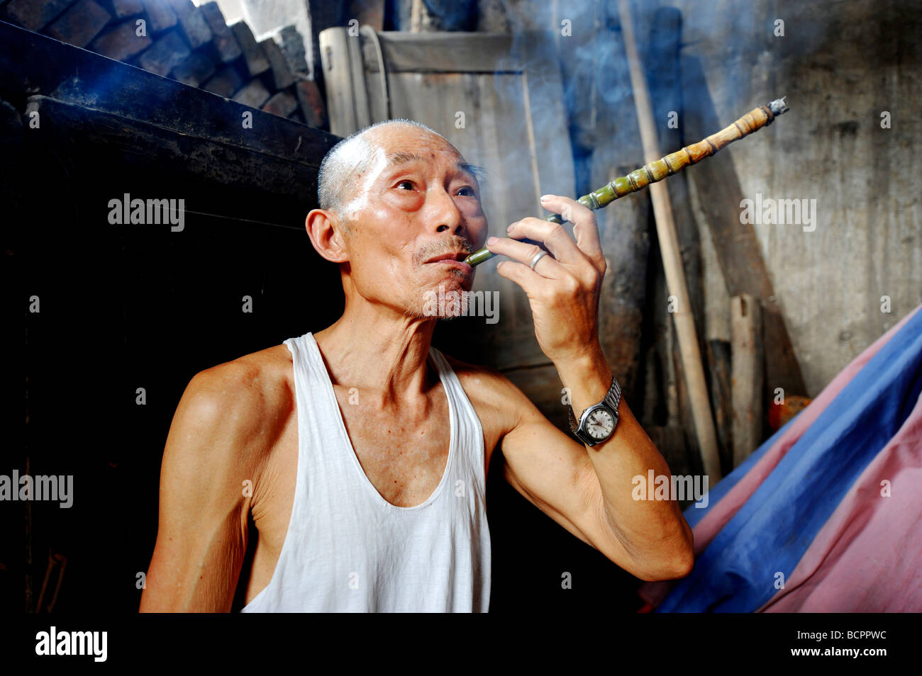 Elderly Chinese man smoking a long pipe made with bamboo, Lizhuang Ancient Town, Sichuan Province, China Stock Photo