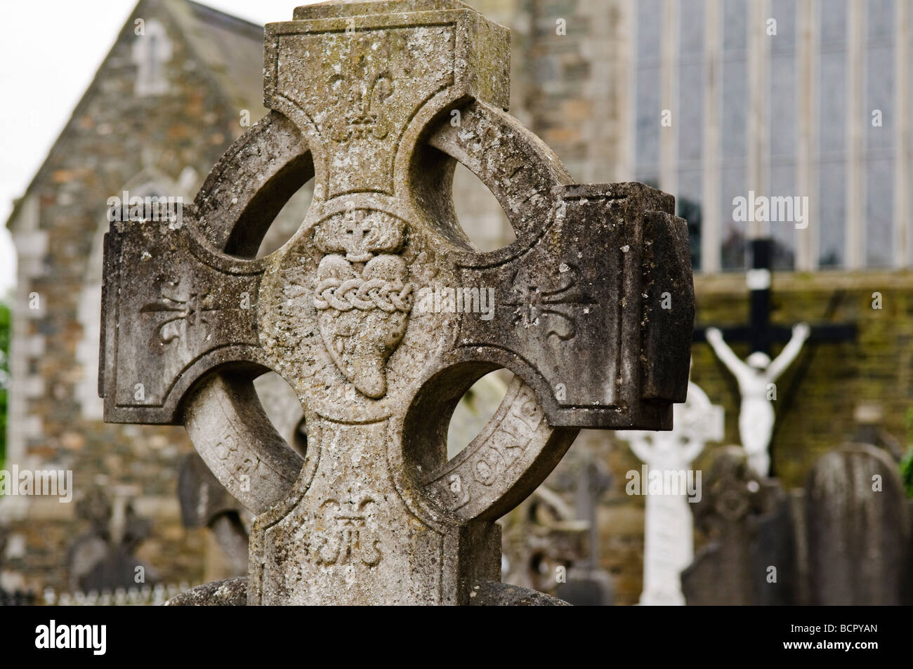 Granite celtic cross with sacred heart carved in centre, in a church graveyard. Stock Photo
