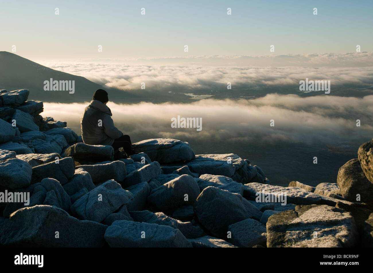 A walker resting at the summit of Cranstackie above low cloud, Sutherland, Scotland, UK Stock Photo