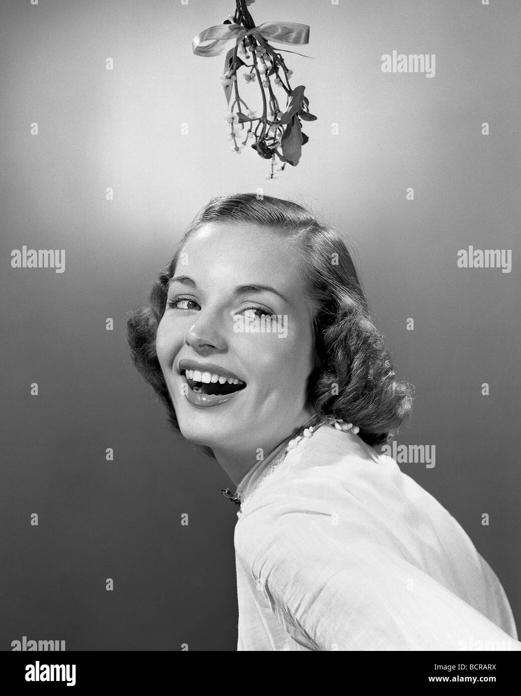 Studio portrait of young woman smiling with mistletoe hanging over her head Stock Photo