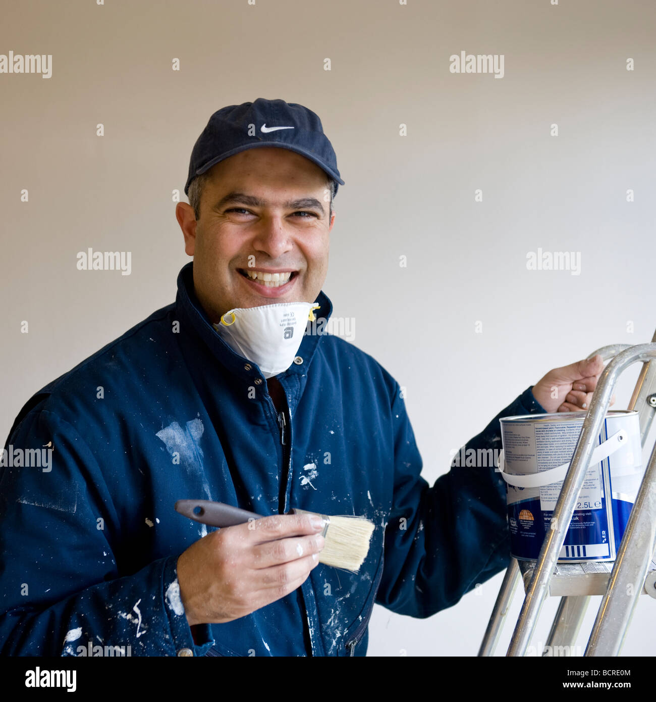 Happy male painter in navy overall, mask, and holding a paint brush