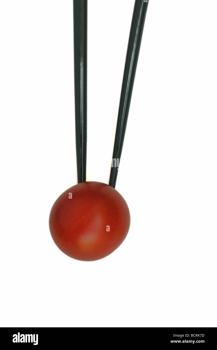 A cherry tomato balanced on the tip of a pair of chopsticks Stock Photo