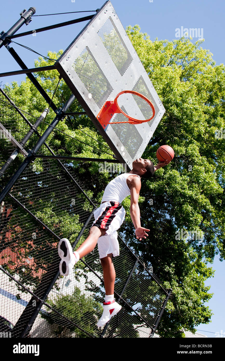 Sporty handsome African American man dressed in white jumping in the air reaching for the basket while playing basketball dunk Stock Photo
