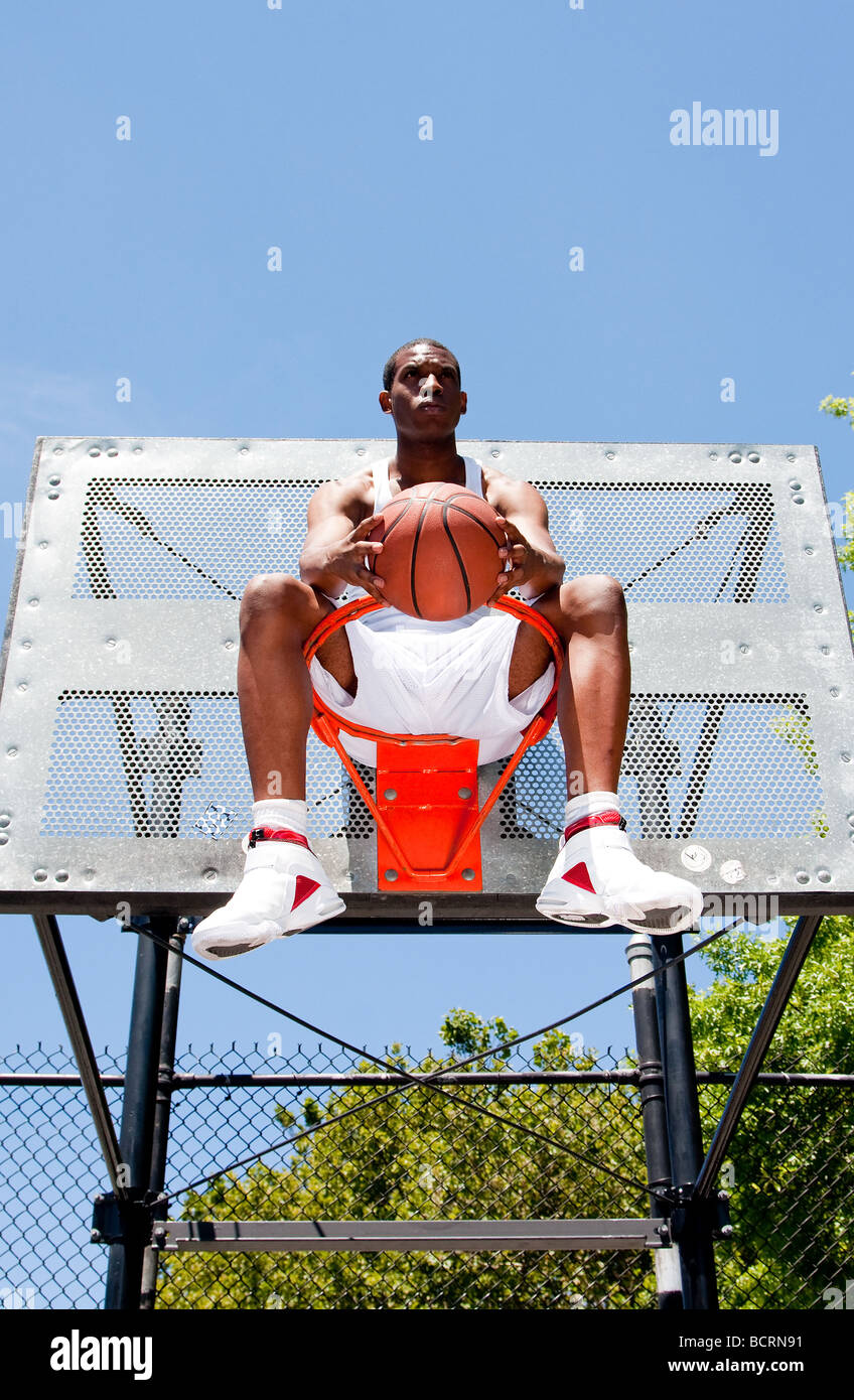 Handsome sporty African American male basketball player dressed in white and holding his ball outdoor on a summer day Stock Photo