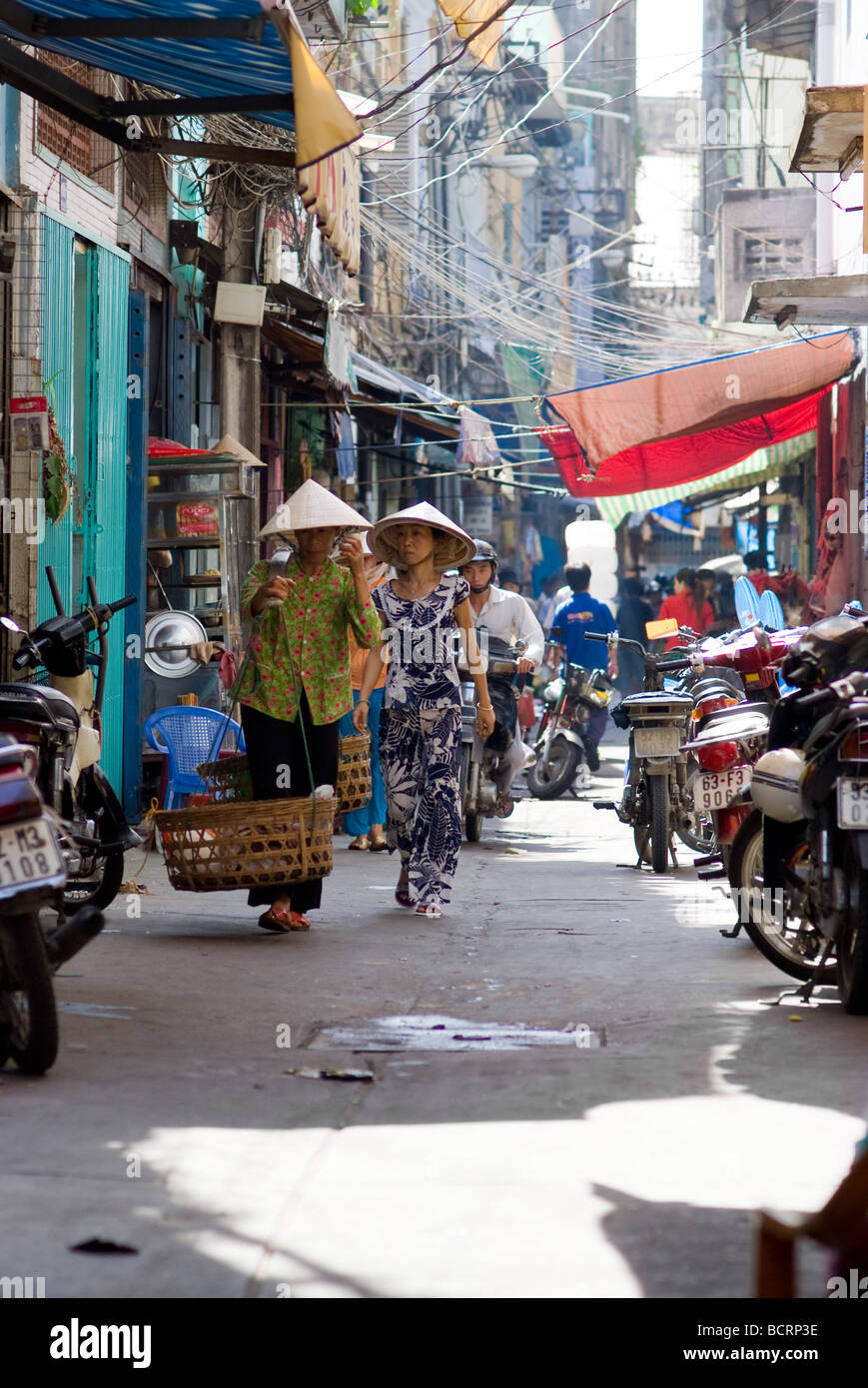 Narrow backstreet with people and motorbikes in Cho Lon the chinatown of Ho Chi Minh City Vietnam Stock Photo