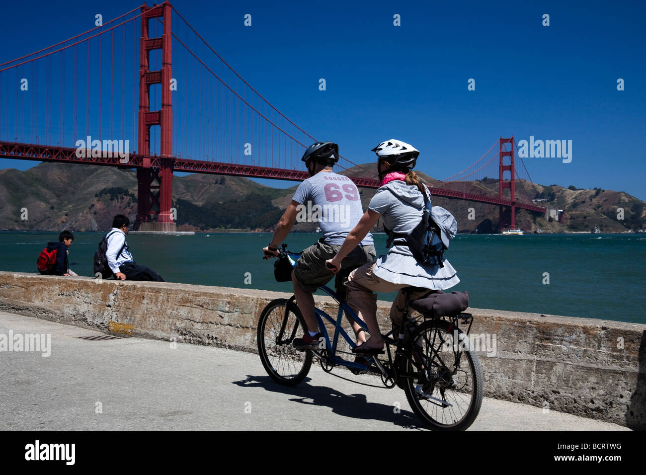 Male and female on Tandem cycle Crissy Field San Francisco, California USA, Golden Gate Bridge in background Stock Photo