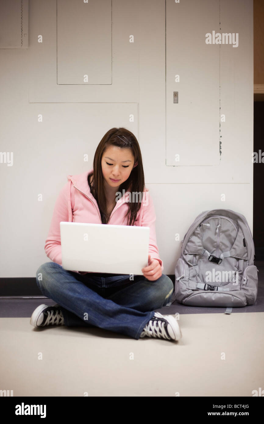 Asian girl using a laptop while sitting on the floor of a campus ...
