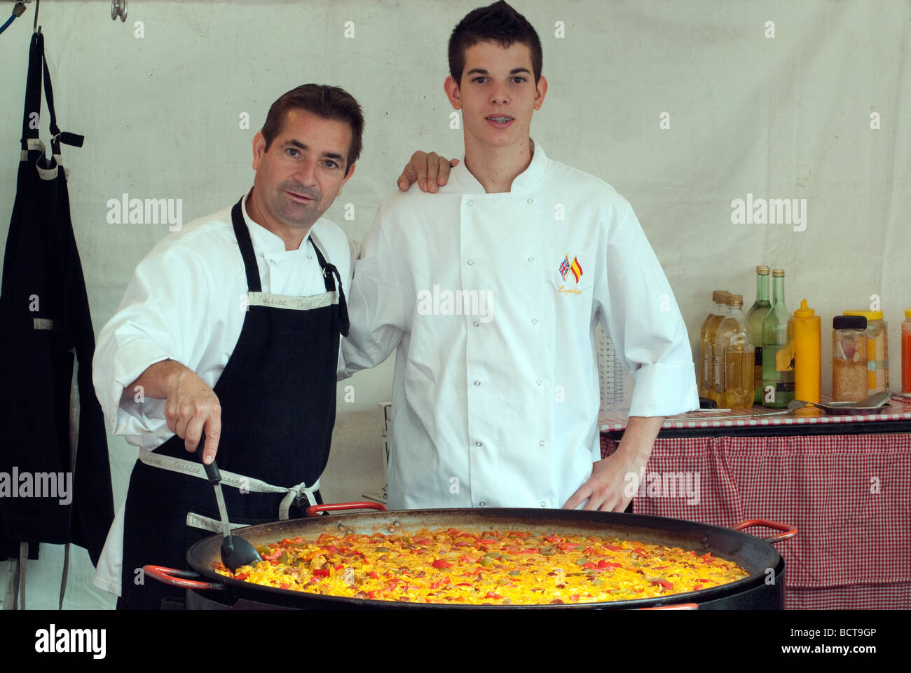 Man and assistant stirring large pan of paella at continental market Stock Photo