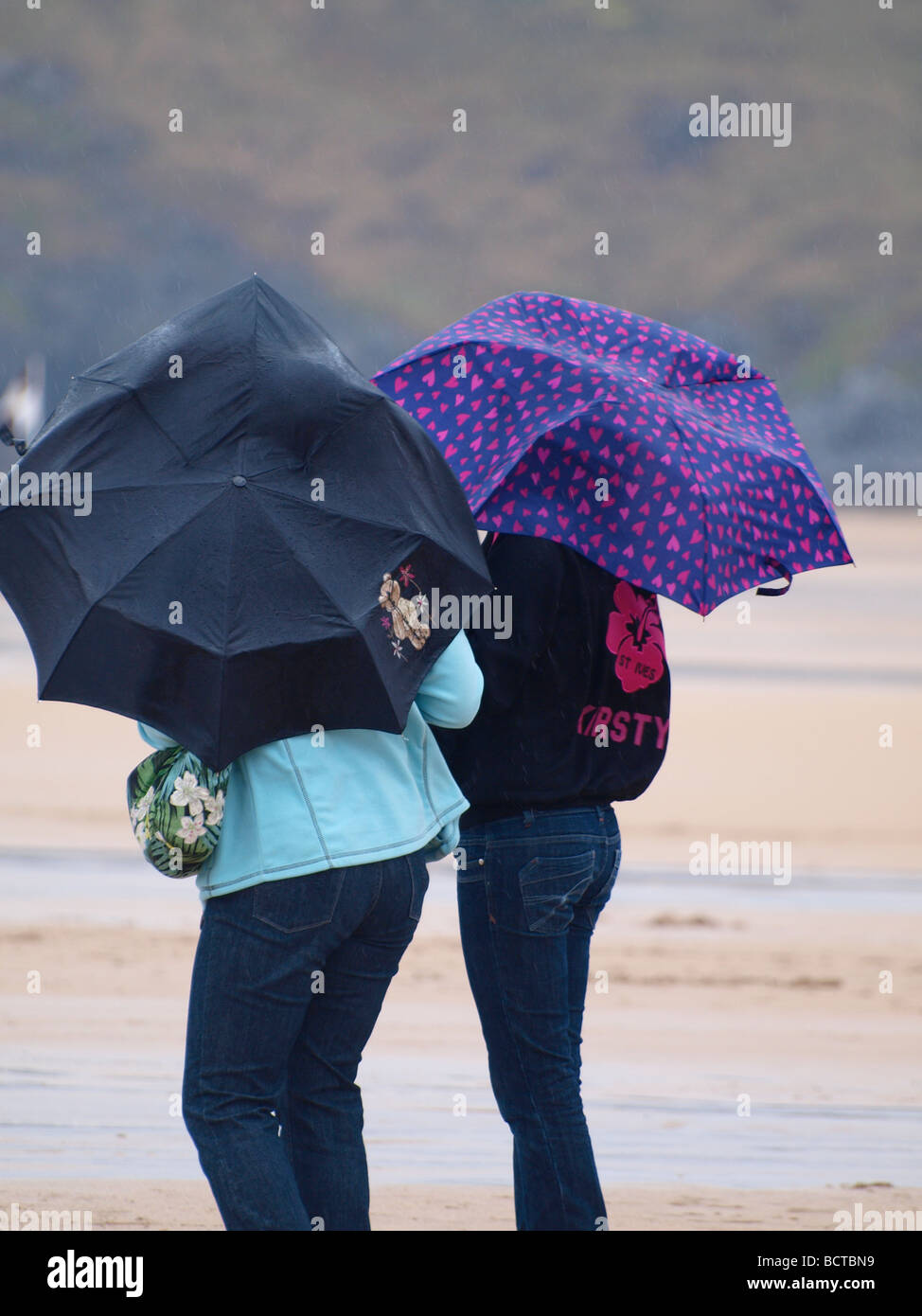 Two woman on the beach on a wet and windy day Stock Photo