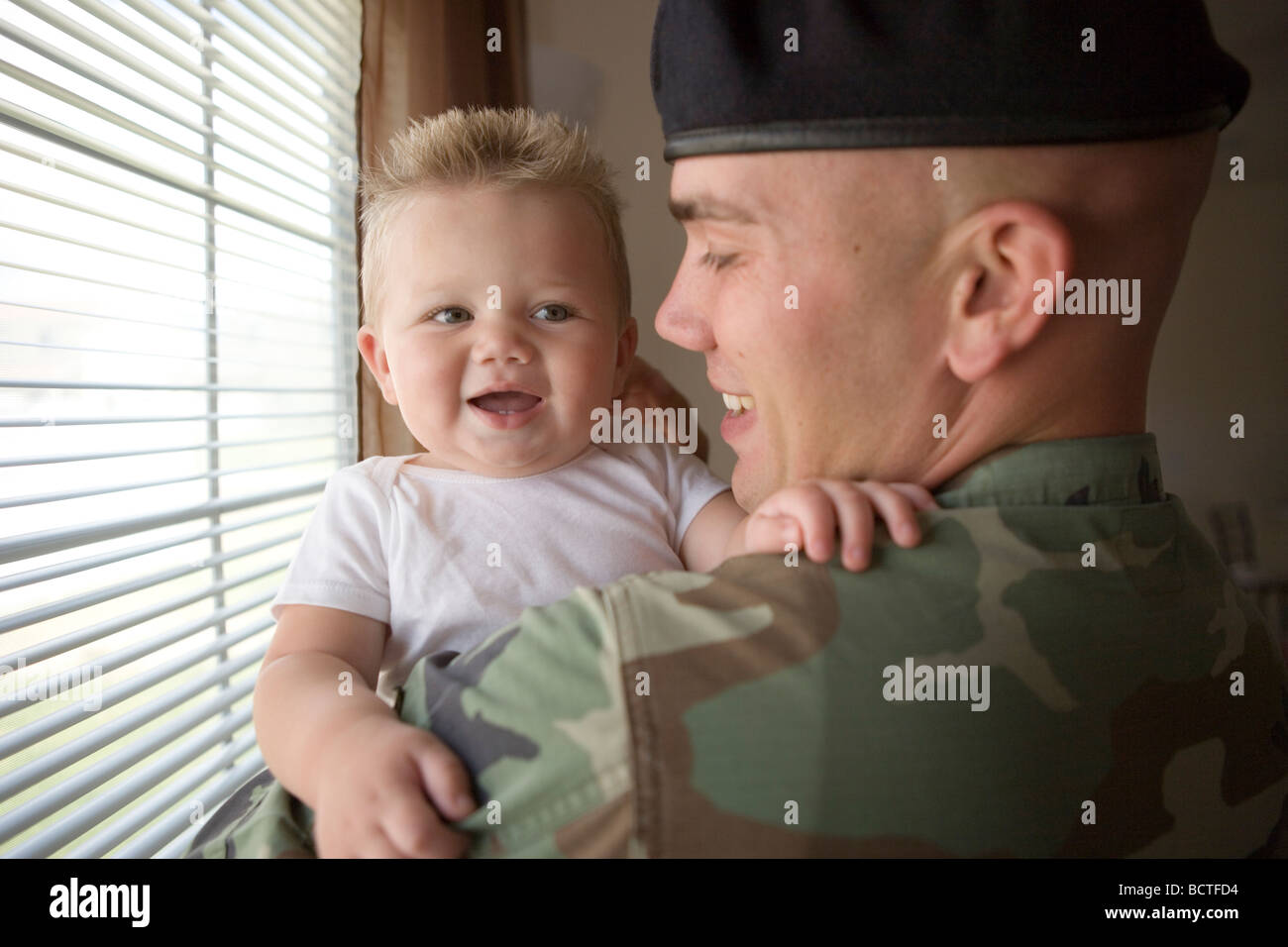american military father coming home and greeting his infant son with a hug Stock Photo