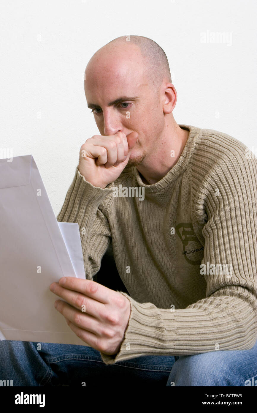 Unhappy man looking at papers in hands, staring at document, could be divorce forms, confusing document or unpaid debts summon. Stock Photo