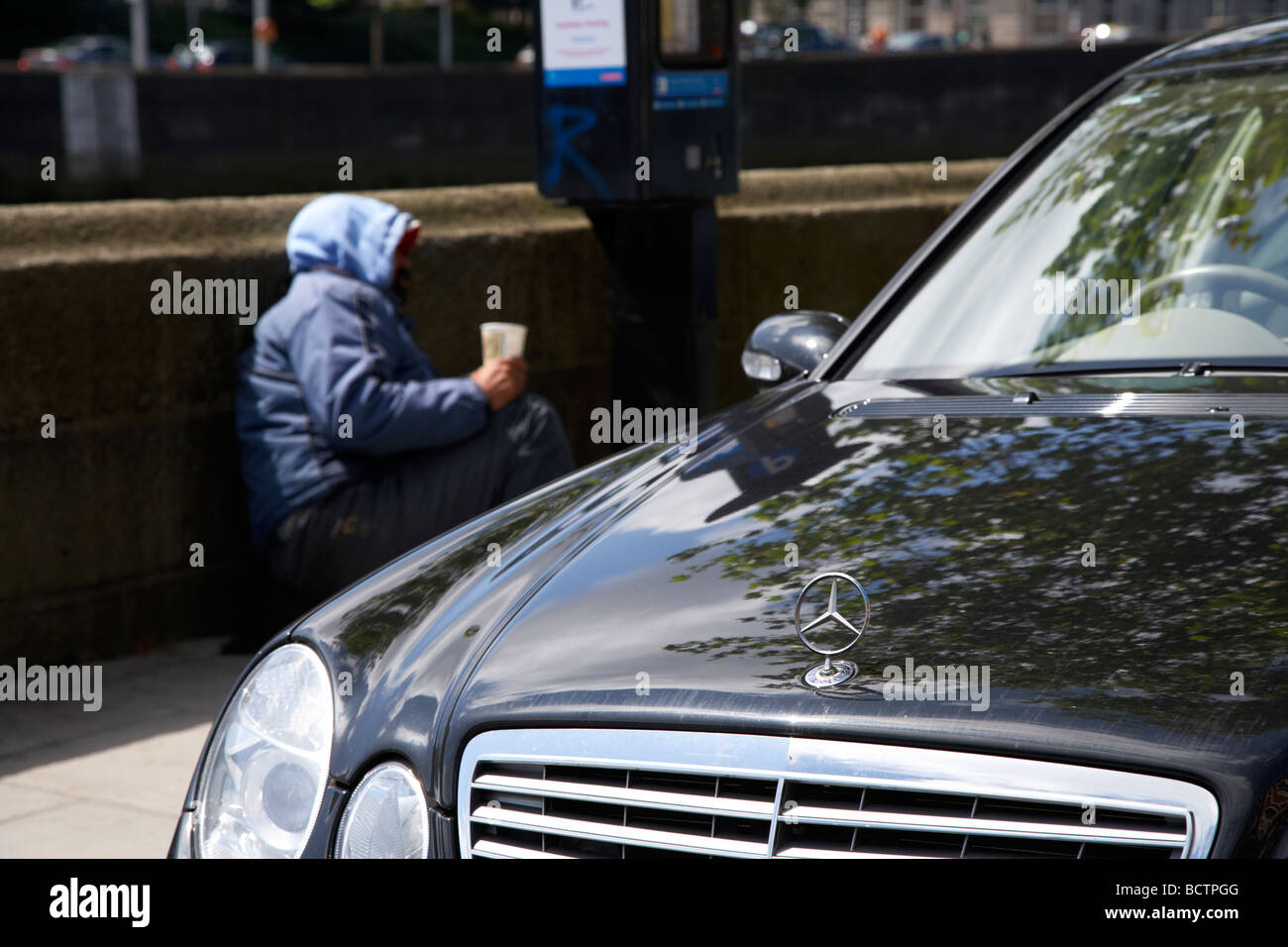 street beggar lying beside a parking ticket machine and mercedes car ...