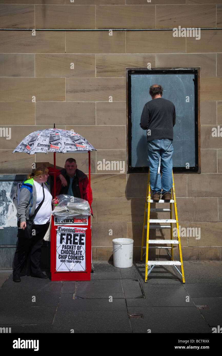 Street scene including a newspaper vendor an obese woman and a bill poster, Glasgow, Scotland, UK Stock Photo