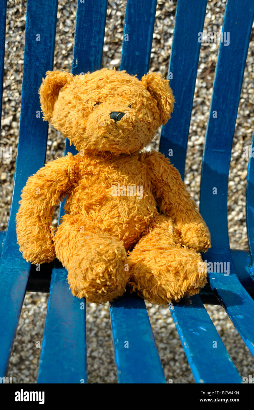 A child's teddy bear seated on a blue summer slatted chair outside. Stock Photo