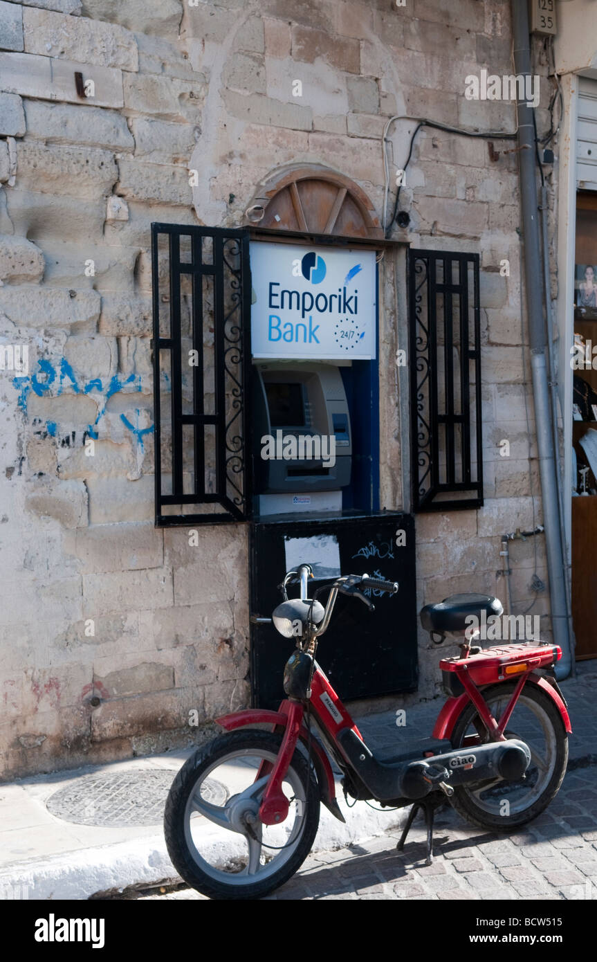 An old moped parked in front of the Emporiki Bank cash machine in the Old Town, Chania, Crete Greece. Stock Photo