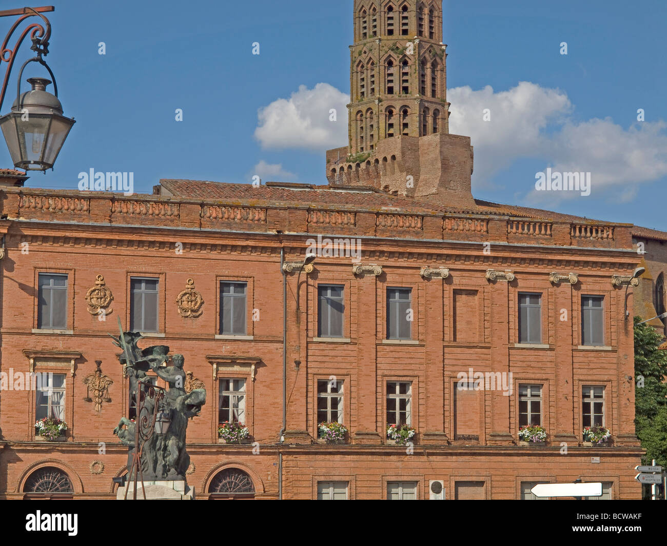 three sculptures two men and one woman with a sword and in background a red church and red stony houses in Montauban in France Stock Photo