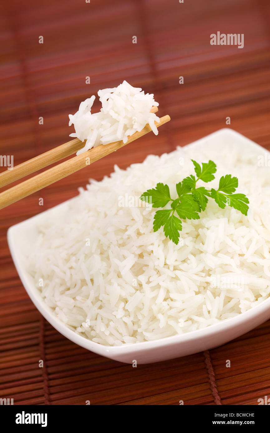 Closeup of rice on chopsticks and a bowl on mat Stock Photo
