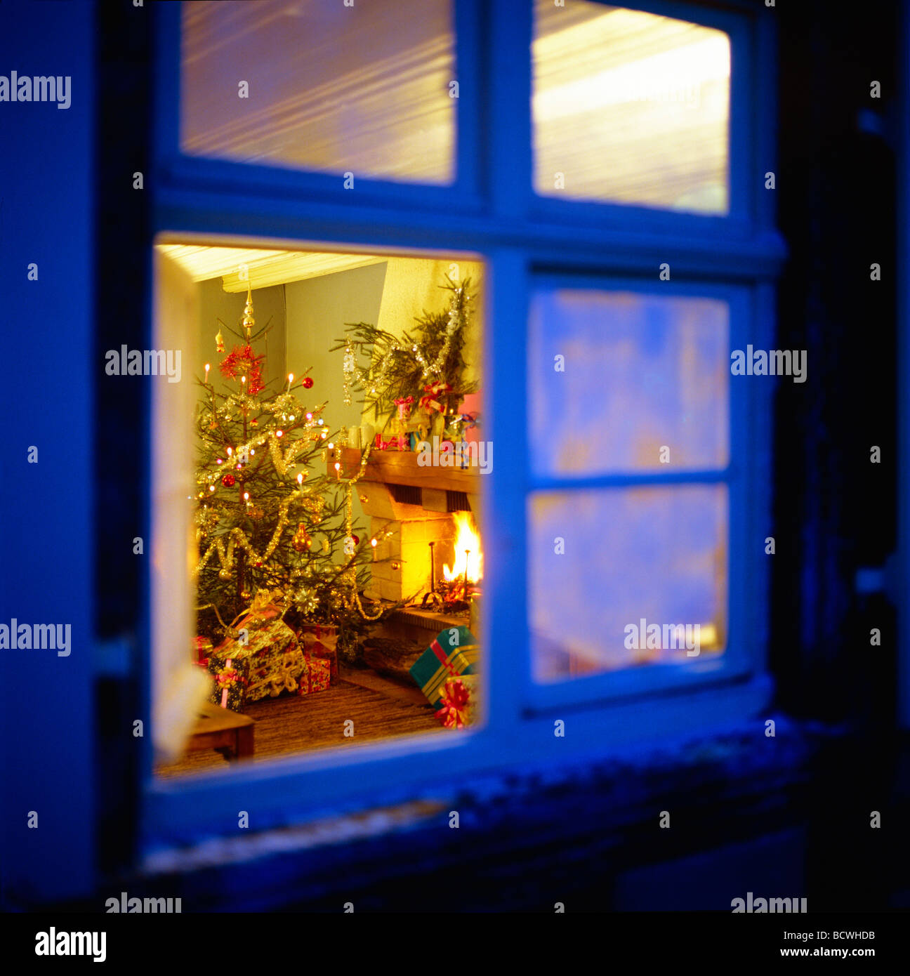CHRISTMAS PRESENTS UNDER THE TREE AND FIREPLACE SEEN THROUGH WINDOW AT NIGHT Stock Photo