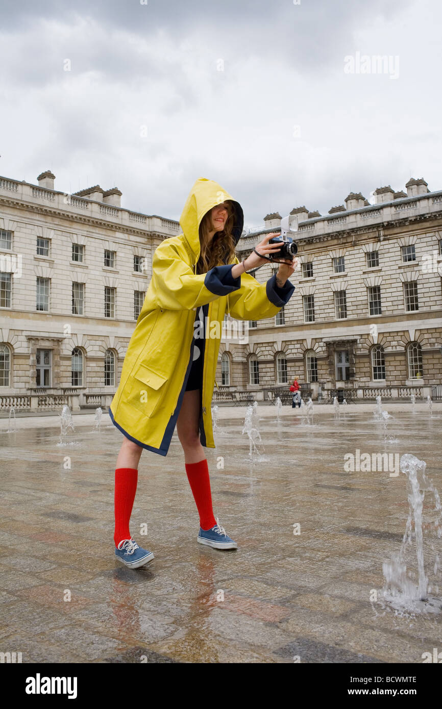 A young woman in yellow waterproof mac coat red socks and blue shoes