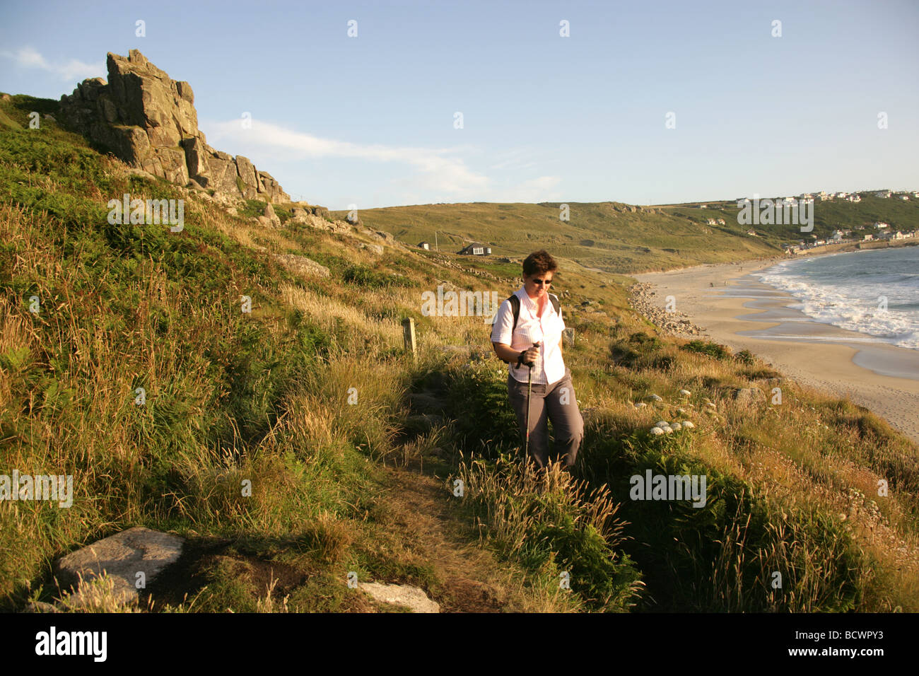 Area of Sennen, England. Lady walking alone along the coastal path with Sennen Cove in the background. Stock Photo