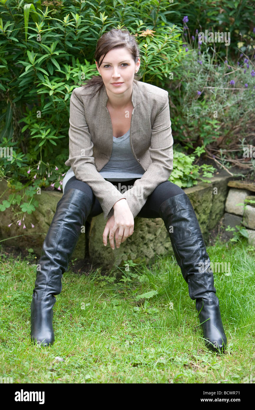 Young woman sitting in garden wearing black boots with legs parted Stock  Photo - Alamy