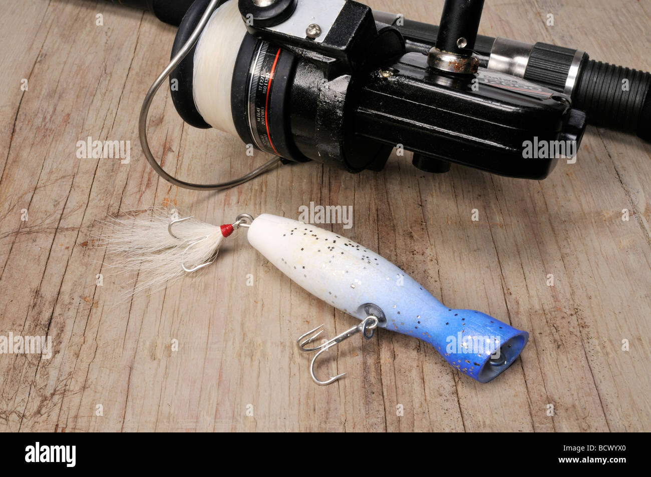Fishing lure with rod, blue and white popper with treble hooks and buck tail and spinning rod & reel on wood Stock Photo