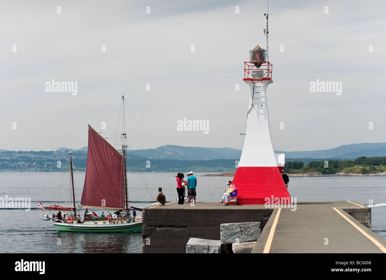 The tall ship 'Thane' sails past the lighthouse guarding Ogden Point on the way to the inner harbor in Victoria, BC. Stock Photo