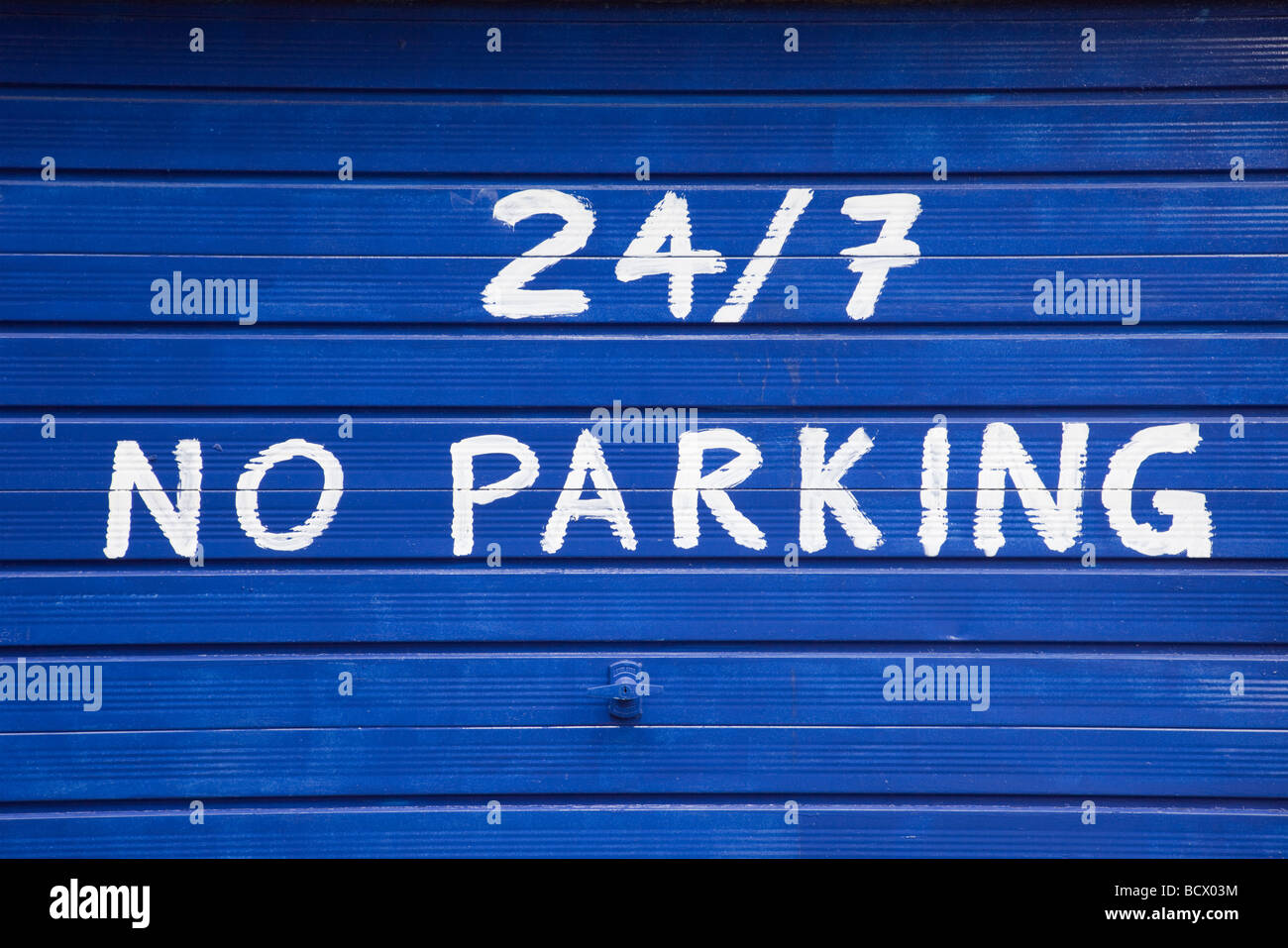 No parking 24/7 sign painted on blue garage door. UK Britain Stock Photo