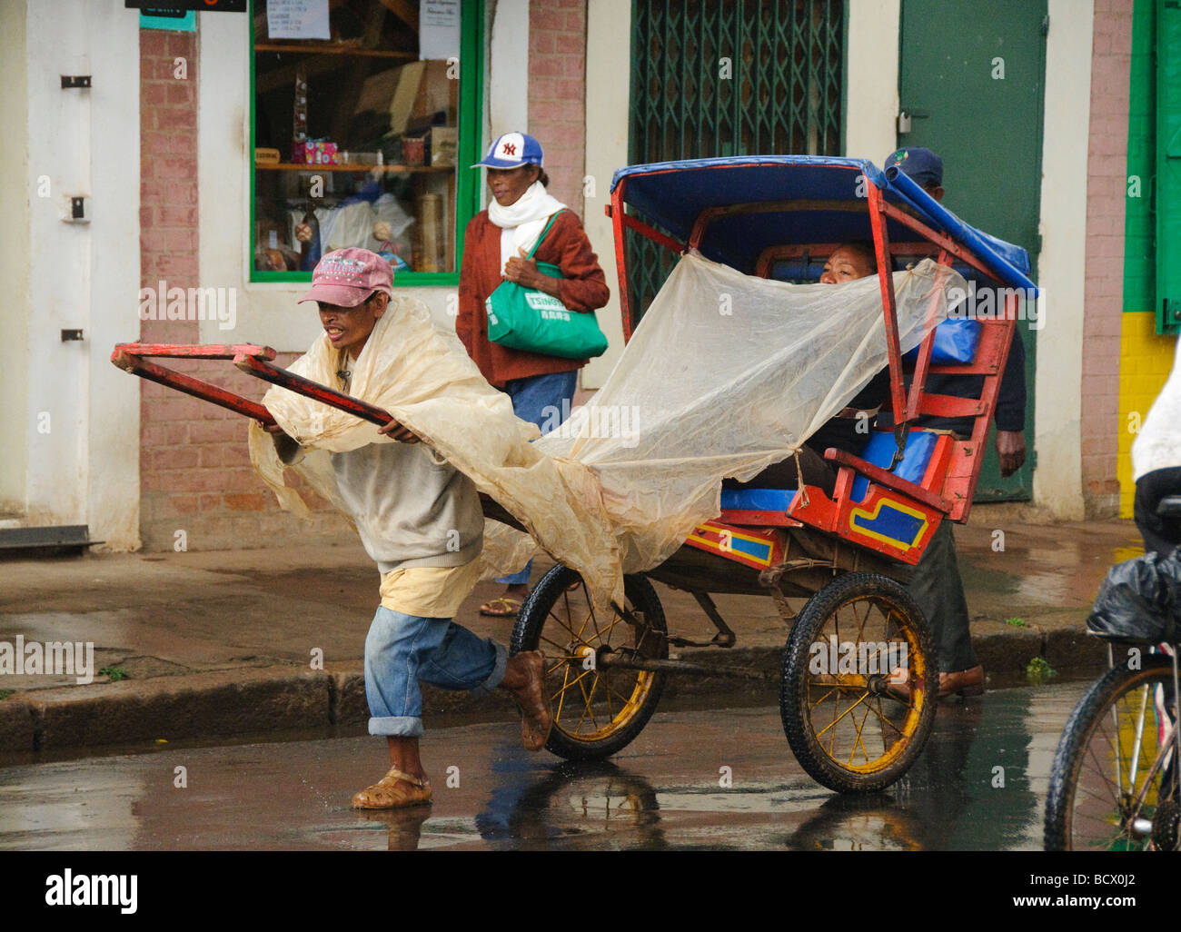 Pousse Posuse pousse pousse driver in the rain in Antisirabe Madagascar Stock Photo ...