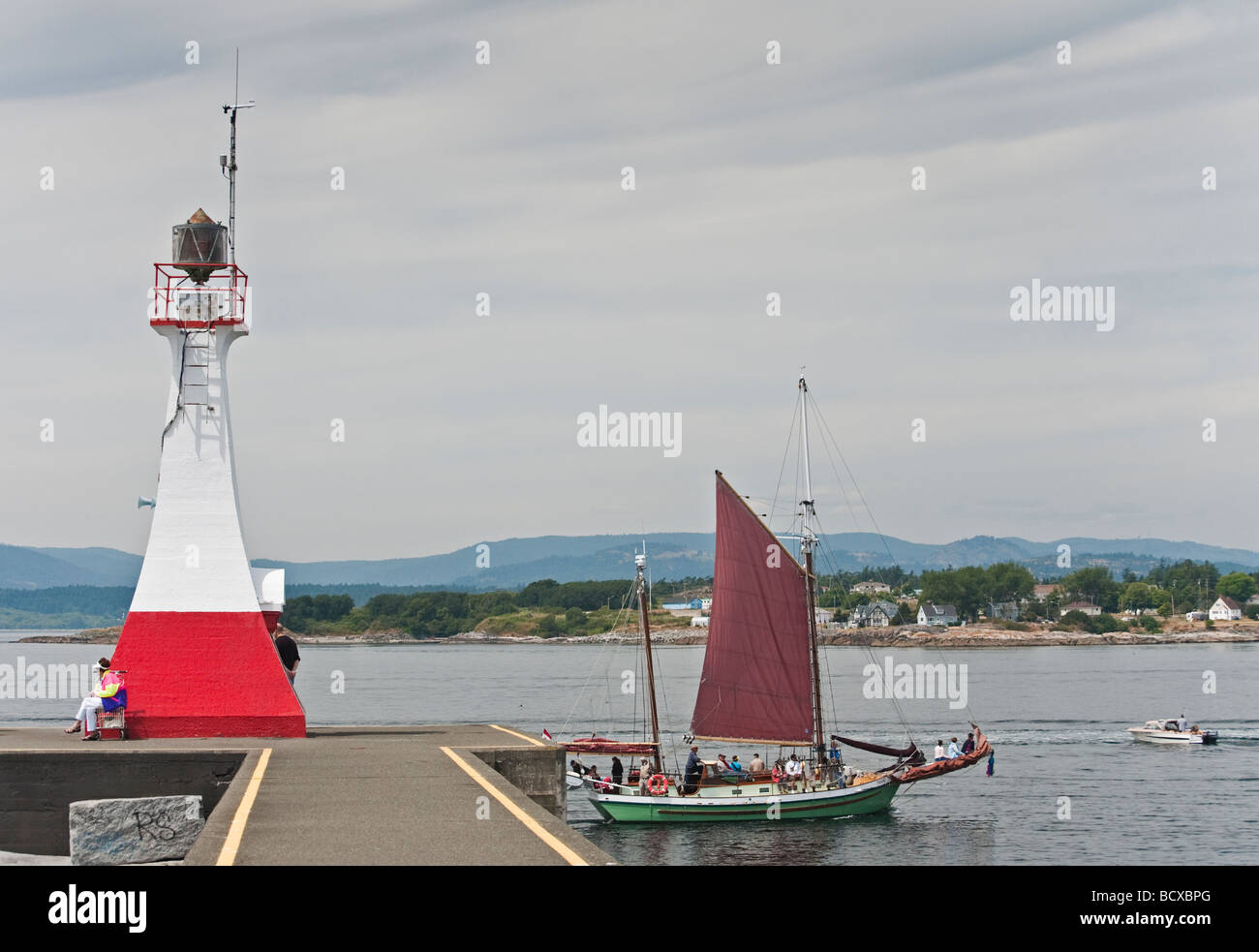 The tall ship 'Thane' sails past the lighthouse guarding Ogden Point on the way to the inner harbor in Victoria, BC. Stock Photo