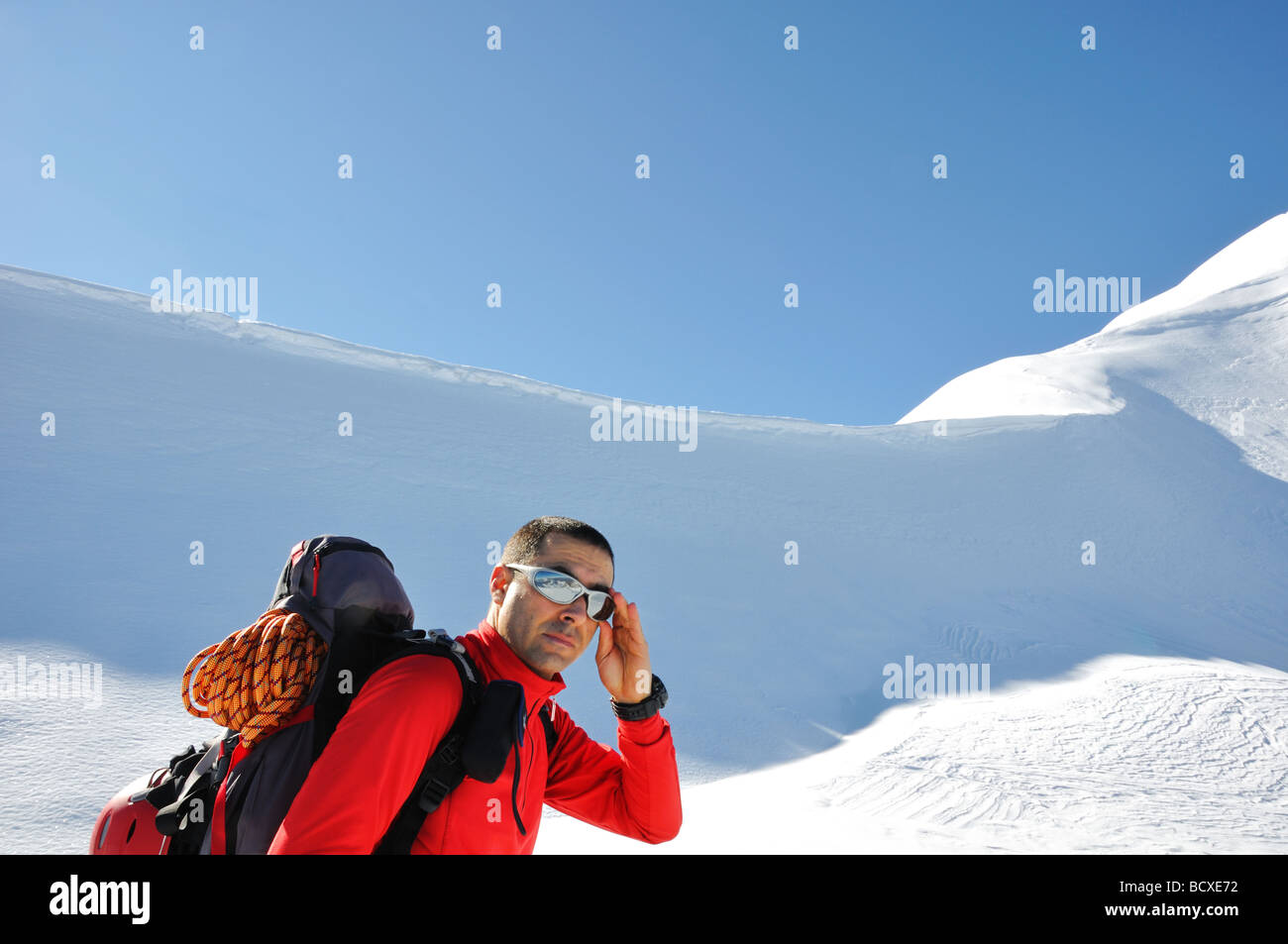 young man with a backpack with climbing gear and equipment just before climbing a mountain ridge covered with snow and ice Stock Photo